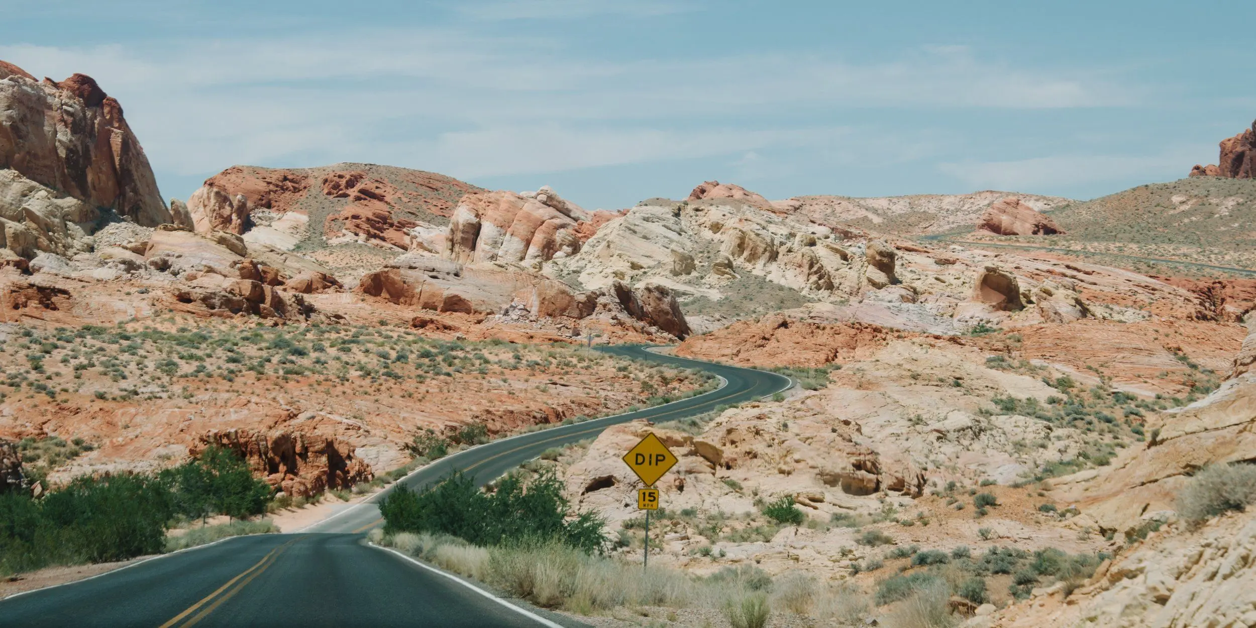 A winding, empty road curves into rocky hills through the Valley of Fire. Midday.