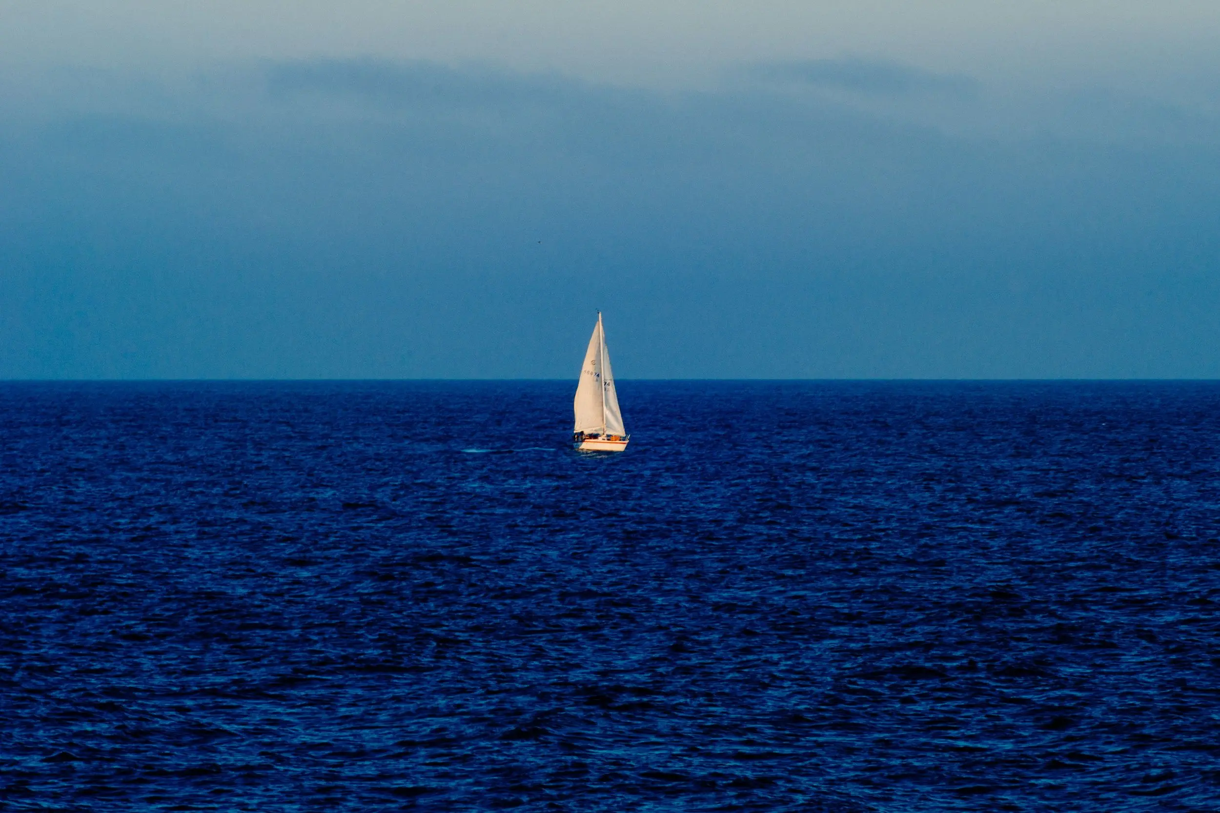 A white sailboat surrounded by the intense blues of the sky and ocean.