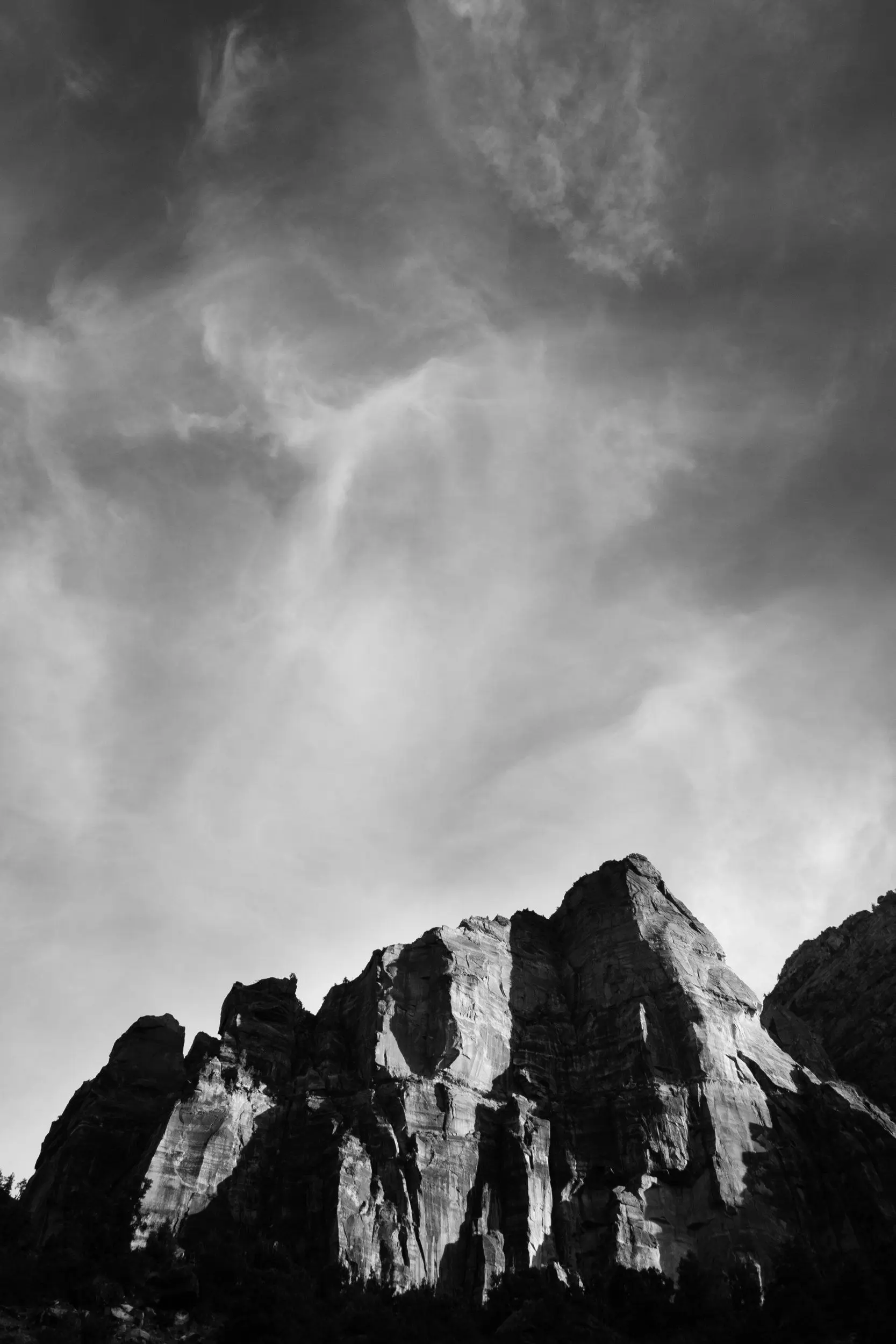 Black and white side-lit from the sunset mountain under wispy clouds on the Zion – Mount Carmel Highway.