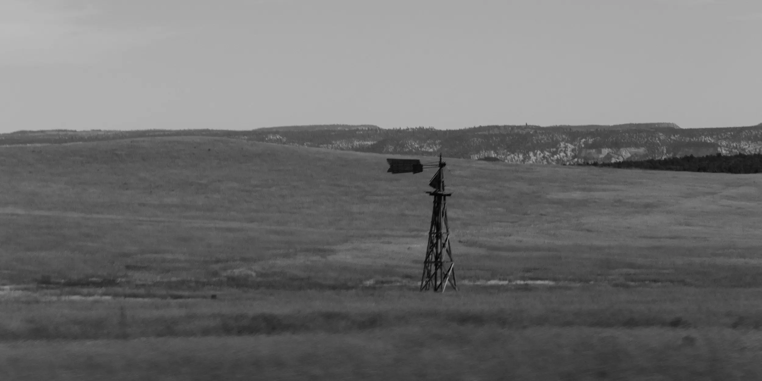 A lone, broken windmill stands in an empty field. Black and white.