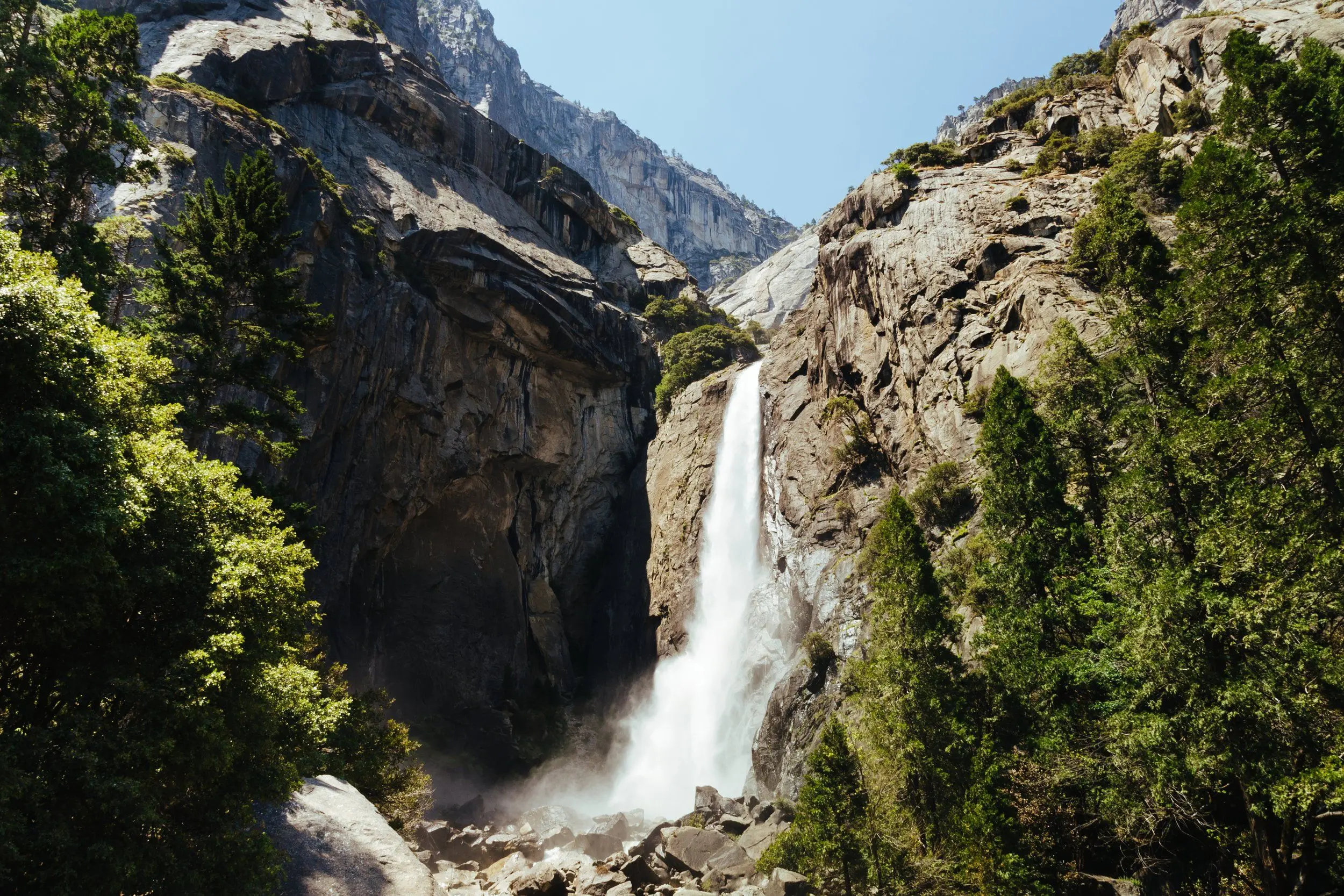 Lower Yosemite Fall surrounded by green trees during midday.